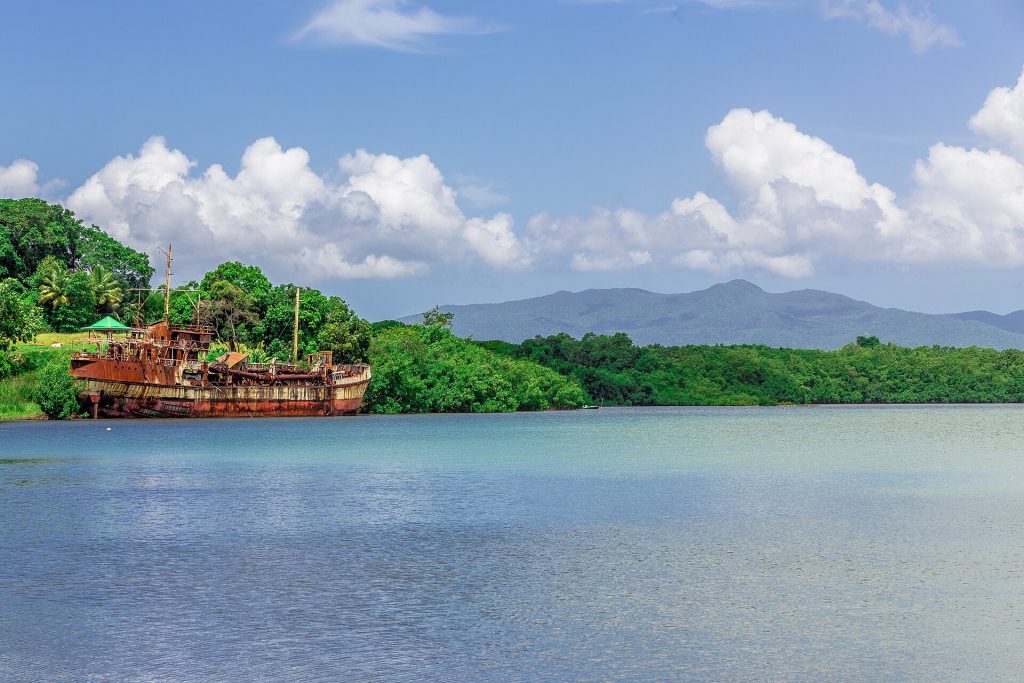 Baie de Baie-Mahault bordée de mangrove, avec une épave rouillée et les monts de Basse-Terre au fond
