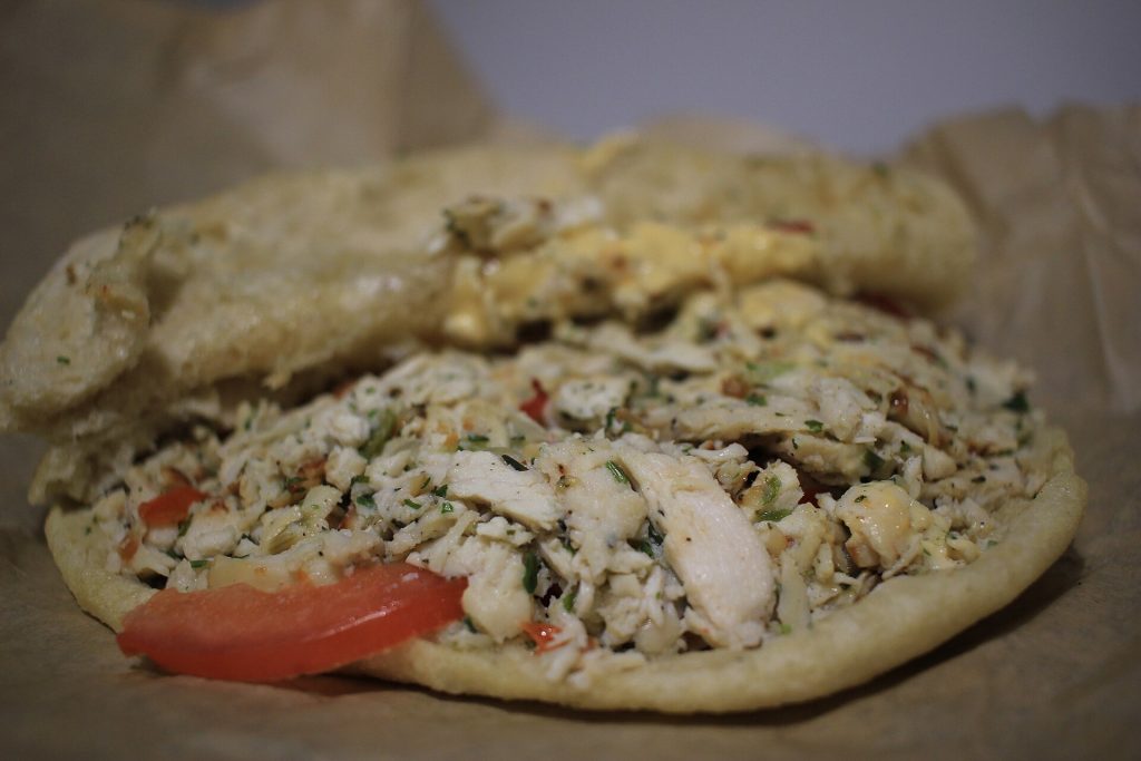 Un bokit au poulet ouvert, garni de poulet effiloché et de tomate