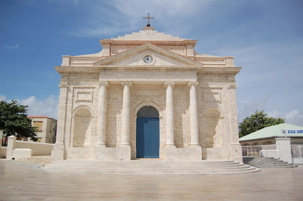 Façade néoclassique blanche de l'église Saint-Jean-Baptiste du Moule sous un ciel bleu