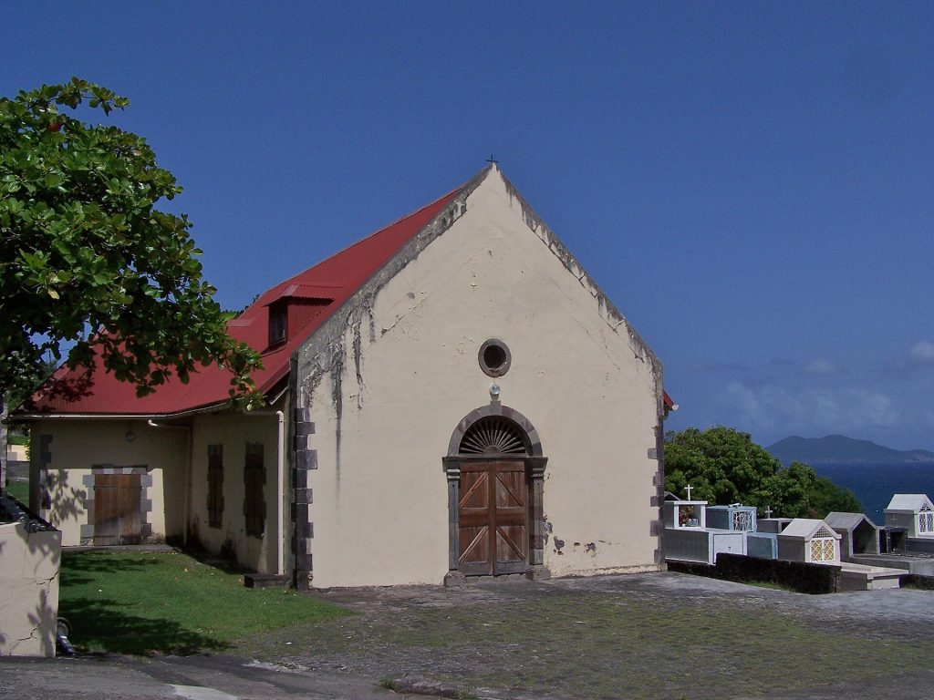 Façade de l'église Saint-Albert de Vieux-Fort, sous un ciel bleu, avec la mer au loin