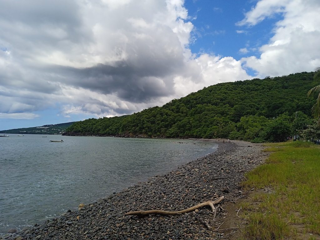 Rivage de galets de la plage Caraïbe à Pointe-Noire, sous un ciel nuageux
